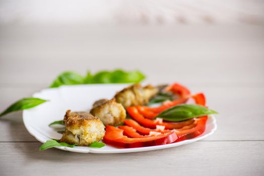 Pieces of fried hake fish in a plate with pepper on a wooden table