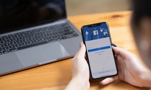 CHIANG MAI ,THAILAND - AUG 18, 2022 : Woman hand holding iPhone X to use facebook with new login screen.Facebook is a largest social network and most popular social networking site in the world..