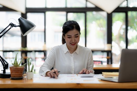Smiling asian business woman working with calculator, business document and laptop computer notebook,financial inspector and secretary making report