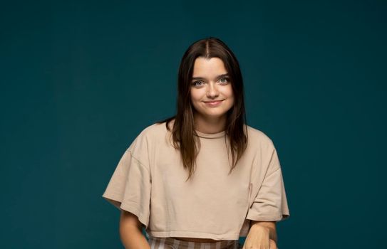 Attractive brunette woman in a beige t-shirt with long hair smiling and looking in a camera