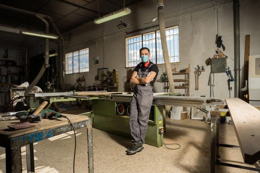 Worker standing with mask and protective gear looking at camera smiling in a factory. Long shot, full body.