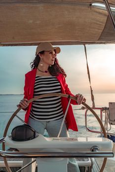 Attractive middle-aged woman at the helm of a yacht on a summer day. Luxury summer adventure, outdoor activities