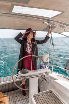 Attractive middle-aged woman at the helm of a yacht on a summer day. Luxury summer adventure, outdoor activities