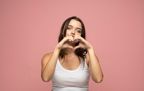 Cute brunette girl wears white t-shirt in love making heart with fingers and smiling. Heart gesture