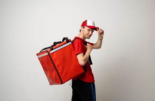 Side view of delivery man in a red uniform carry thermal backpack full of food, groceries to the clients. Food delivery service