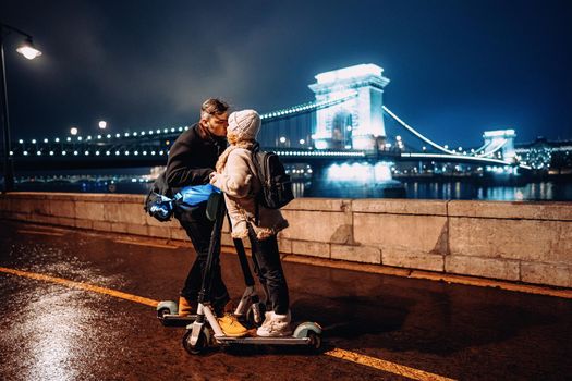 Young happy couple kissing with electric scooter outside in front of ancient european bridge in winter