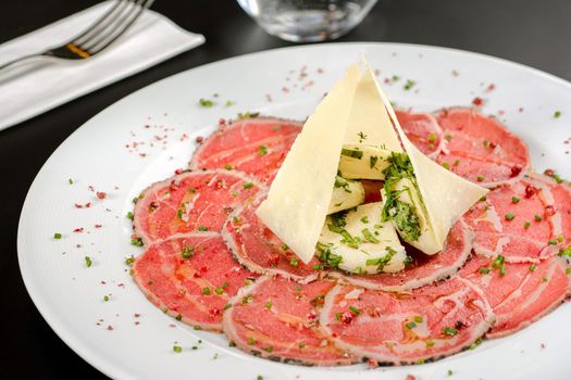 Beef Carpaccio cold appetizer with parmesan, capers and arugula on white plate.