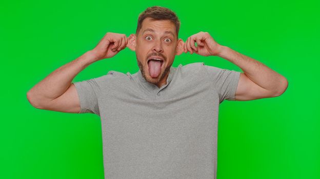 Bearded handsome funny man in t-shirt making playful silly facial expressions and grimacing, fooling around, showing tongue. Adult male guy isolated alone on chroma key studio background indoors