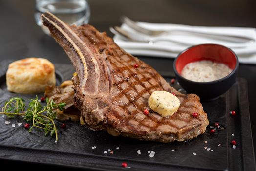 Grilled veal cutlet on black stone plate with sauce and garnish.