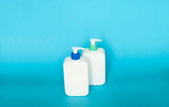 White cosmetic plastic bottles with black pump dispenser on blue background. Liquid containers for gel, lotion, cream, shampoo, bath foam