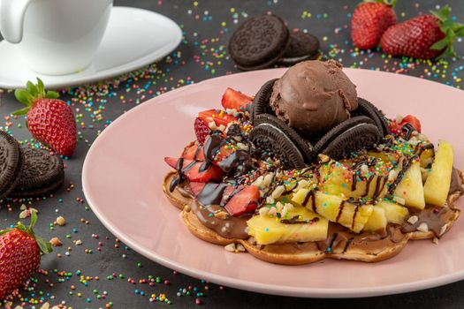 Heart waffle with pineapple and strawberry with gummy candy and ice cream on it.