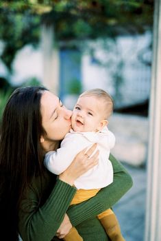 Mom kisses a smiling baby in her arms. High quality photo