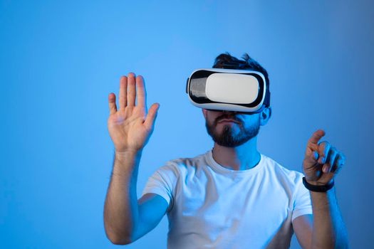 Young bearded man in VR helmet playing VR games on colourful background. VR gaming