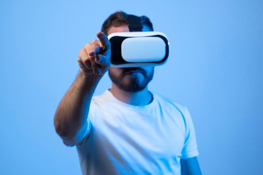 Mature bearded man interacting with the metaverse while wearing virtual reality goggles. Young man using his finger to press a virtual button