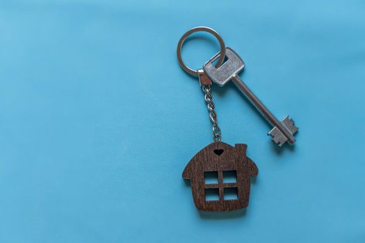 Key with a house keychain on a colored blue background. Real estate agent. Buying a house, apartment