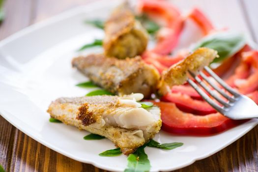 Pieces of fried hake fish in a plate with pepper on a wooden table