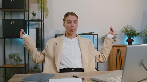 Businesswoman working on laptop computer, meditating, doing yoga breathing exercise in lotus position at home office desk. Calm serene freelancer woman taking break. Busy occupation. Peace of mind