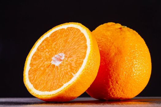 Half an orange. Two halves of fruit on a wooden table. Fresh and ripe fruit is cut on a dark background. Copyspace.