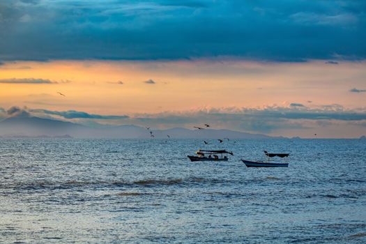 Evening view of the Pacific Coast of Tarcoles in Carara with sunset and glittering waves . Idyllic sunset landscape with fishing boats. Tarcoles, Costa Rica. Pura Vida concept.