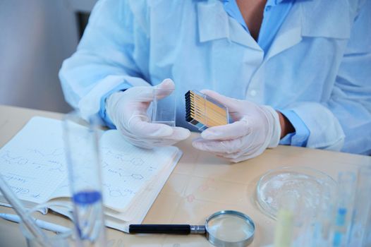 Details: Scientist chemist hands in medical gloves holding a container with litmus or reagent paper for measuring the PH, alkalinity and acidity of substances in chemical research laboratory. Close-up