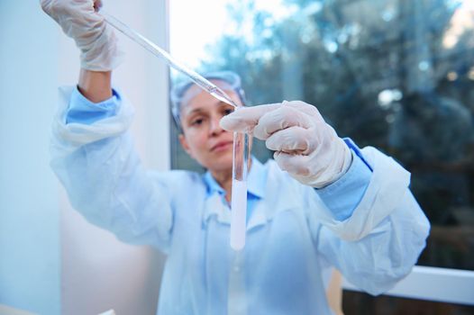 Selective focus. Test tube with a chemical substance in the hands of a chemist, using a graduated pipette and titrating a reagent in a medical science laboratory, while conducting a clinical study