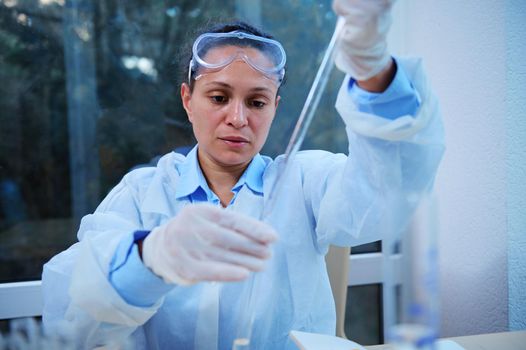 Multi-ethnic woman scientist, pharmacologist with a test tube and a pipette in her hands. A laboratory assistant drips a clear liquid into a test tube with a special preparation. Scientific experiment