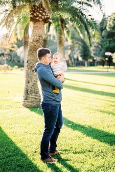 Dad with a baby in his arms stands under a palm tree. High quality photo