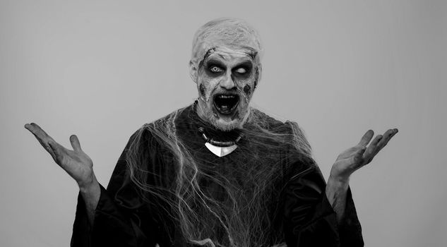 Oh my God, Wow. Frightening man with Halloween zombie bloody wounded makeup raising hands in surprise looking at camera with big eyes, shocked by sudden victory. Excited amazed sinister undead guy