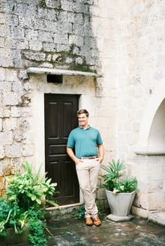 Young man stands near the door of an ancient stone building. High quality photo