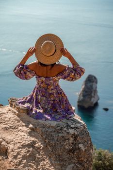 Rear view of a woman sitting in a colorful dress and hat looking towards the blue ocean and sky, isolated sea background.