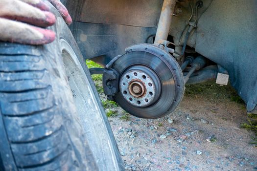 Tire wheel with missing cap cover on parked car with man replacing hubcap with new shiny metal outside. High quality photo