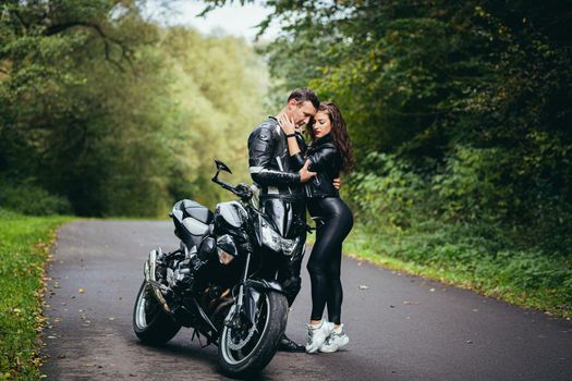 Handsome young man and beautiful young girl, couple sitting on a motorcycle, standing near a motorcycle in black leather clothes, hugging, in nature, on the street