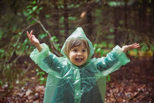 Charming child in a raincoat in the evening forest in Denmark