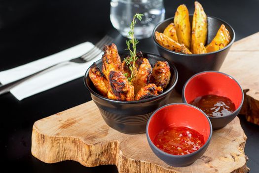 BBQ chicken wings with dip sauce and french fries. close-up of wooden tray with selective focus.