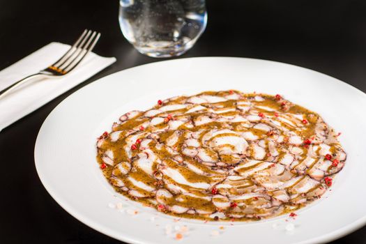 Octopus Carpaccio. Seafood raw octopus slices with olive oil and black pepper on a white plate.