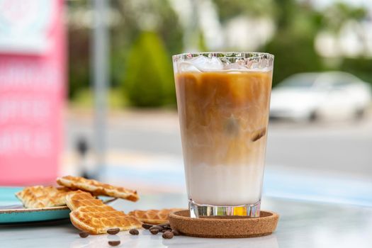 A cup of Iced Latte Coffee with ice cubes placed on a marble table in a coffee shop.