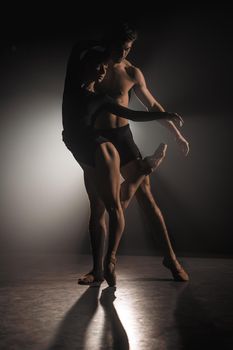 Beautiful young acrobats or gymnasts on floodlights background. Professional ballet couple dancing in spotlights smoke on big stage. Emotional duet performing choreographic art.