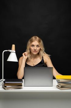 Portrait of attractive freelancer woman in a black t-shirt with a laptop in a studio with a black wall