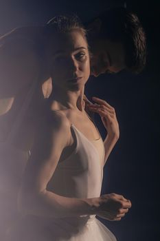 Romantic professional ballet pair practicing moves on dark stage. Young couple dancing in classic dress, spinning around and smiling. Gracefulness and tenderness in every movement