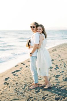 Young woman hugging a man from behind while standing on the beach by the sea. High quality photo