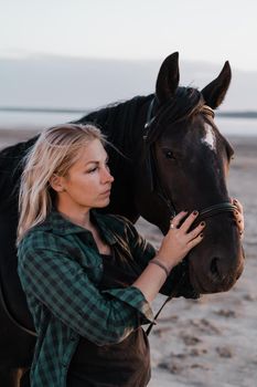 Blonde woman stroking and hugging horse. Beautiful lady with black stallion enjoying sunset nature. Love and friendship concept