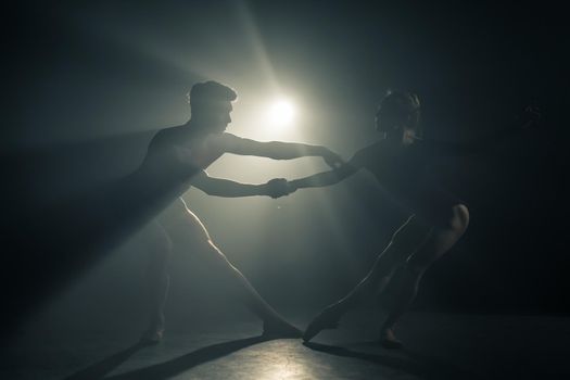 Professional ballet couple dancing in spotlights smoke on big stage. Beautiful young woman and man on floodlights background. Emotional duet performing choreographic art