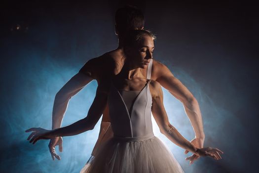 Graceful ballerina and her male partner dancing elements of classical or modern ballet in dark with floodlight backlight. Couple in smoke on black background. Art concept