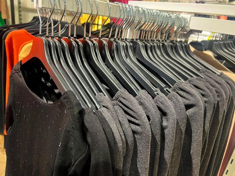 clothes on a rack in a store. Wardrobe with same black dresses and t-shirts. black women's Fashion clothes hanging on hangers. Closeup on group of accessory, household showroom department
