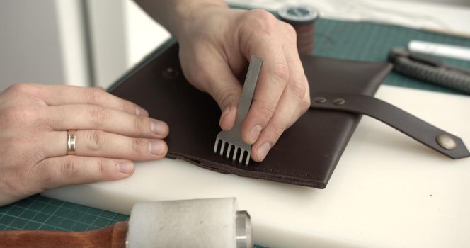 Making of brown handmade leather wallet. Sewing wallet. Piercer punches holes in a piece of skin
