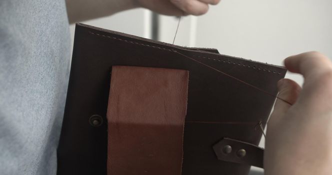 Making a handmade brown leather wallets. The hands of the master sew a leather product