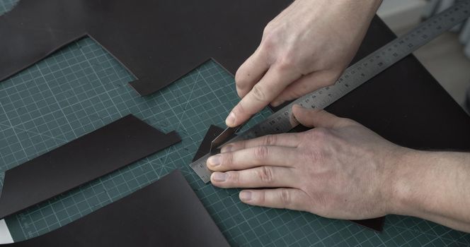 Leather craftsman working with brown natural leather work with knife and metal ruler and cutting a brown leather to a pieces. Handmade concept. Concept of small business to create leather products