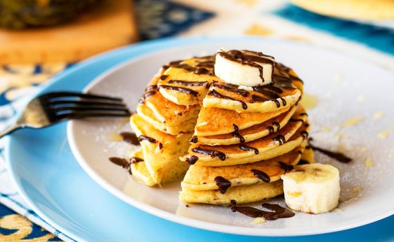 classic american breakfast. homemade banana pancakes on plate sprinkled powder and honey. A slide of hot pancakes with fresh bananas on a plate on the kitchen table . Pancake slide with honey topping