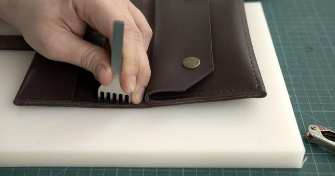 Craftsman making holes in leather with puncher tool. Working process with a brown natural leather