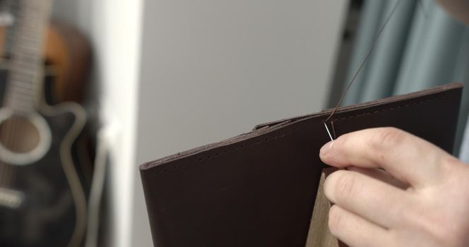 Sewing a brown leather wallet. Leather work. Sewing products by hand. Manufacture of leather goods